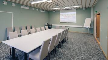 Een vergaderruimte met een lange tafel, stoelen, een scherm voor een beamer en een whiteboard.