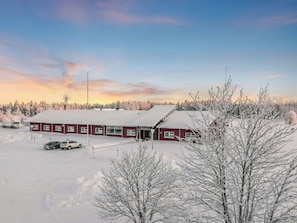 Un bâtiment rouge, doté d’un toit plat, entouré d’arbres couverts de neige et surplombant un ciel dégagé.