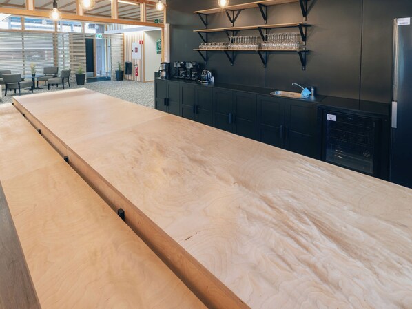 A billiards table in a modern kitchen with a coffee machine, shelves with glasses, and a refrigerator.