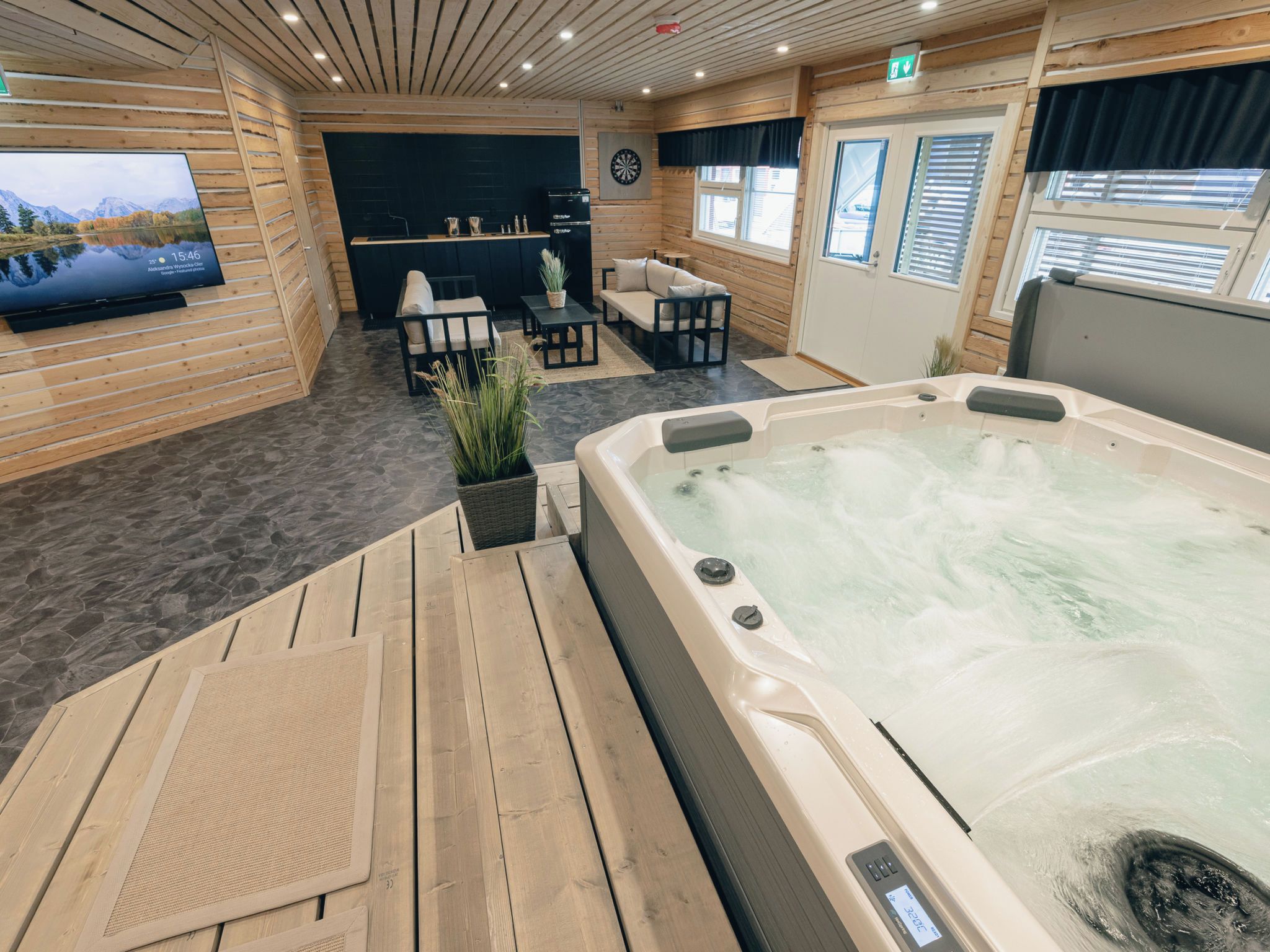 Ein Bereich mit Whirlpool, Holzboden, einem an der Wand montierten Fernseher und einer Sitzecke mit Couch und Sesseln.