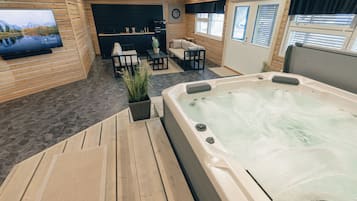 Ein Bereich mit Whirlpool, Holzboden, einem an der Wand montierten Fernseher und einer Sitzecke mit Couch und Sesseln.