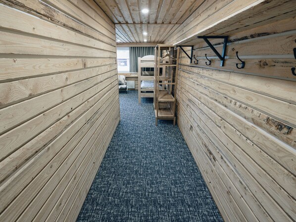 Un couloir étroit aux murs en bois et au sol recouvert d’une moquette, qui mène à un espace avec des lits superposés.