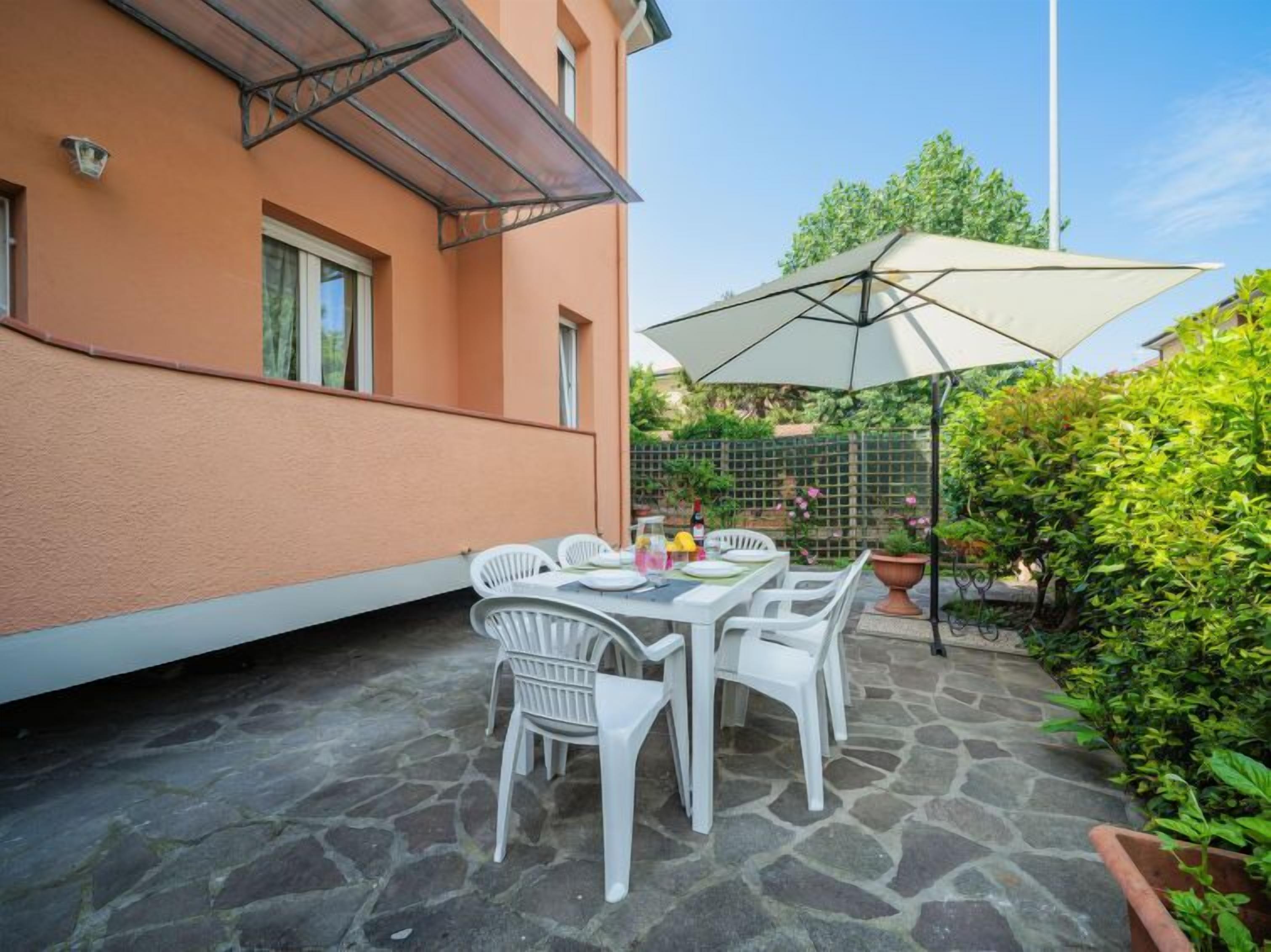 Un patio al aire libre con piso de piedra, sillas de plástico blanco y una mesa lista para comer.