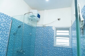 Een badkamer met een douchecabine van glas, een raam en blauwe betegelde wanden.