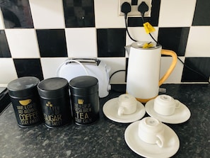 A kitchen counter with a coffee maker, two black containers with coffee and tea labels, a toaster, and white tea cups and saucers. - Lovely 3-bed Charming Apartment in Portsmouth (Portsmouth)
