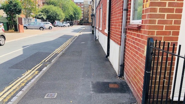A narrow sidewalk adjacent to a brick building with a black metal fence.