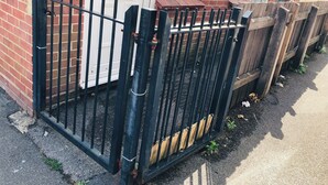 A black metal gate with vertical bars, a brick wall, and a white door.