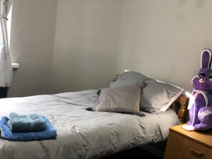 A bed with grey bedding, a blue pillow, and a purple stuffed toy on a wooden nightstand. - Lovely 3-bed Charming Apartment in Portsmouth (Portsmouth)