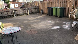 A paved patio with a mosaic table, a metal chair, and a wooden fence.