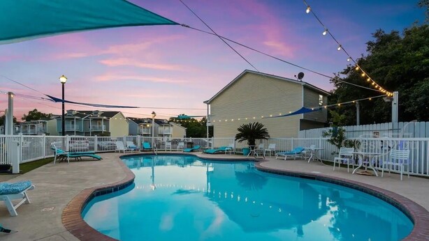 A swimming pool with lounge chairs and string lights, surrounded by a white fence and a building. - Beach Sand House, Sleep 8, Swimming Pool, Gated E (Gulfport)
