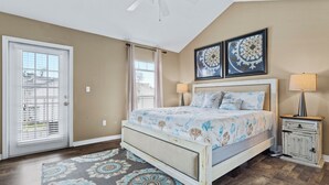 A bedroom with a bed, a nightstand, a lamp, a door with blinds, and a ceiling fan. - Beach Sand House, Sleep 8, Swimming Pool, Gated E (Gulfport)