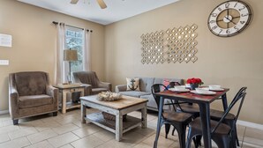 A living room with a sofa, armchairs, a coffee table, and a dining table with chairs. There is a wall clock and a decorative wall piece. - Beach Sand House, Sleep 8, Swimming Pool, Gated E (Gulfport)