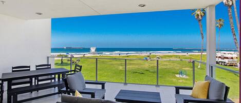 Een balkon met uitzicht op het strand, buitenmeubilair en een heldere lucht.