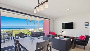 A modern living area with a dining table, sofas, a TV, and a view of the ocean. - Stylish Ocean Front Condo with Great Views (San Diego)
