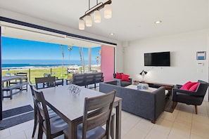 Een moderne woonkamer met een eettafel, banken, een televisie en uitzicht op de oceaan.