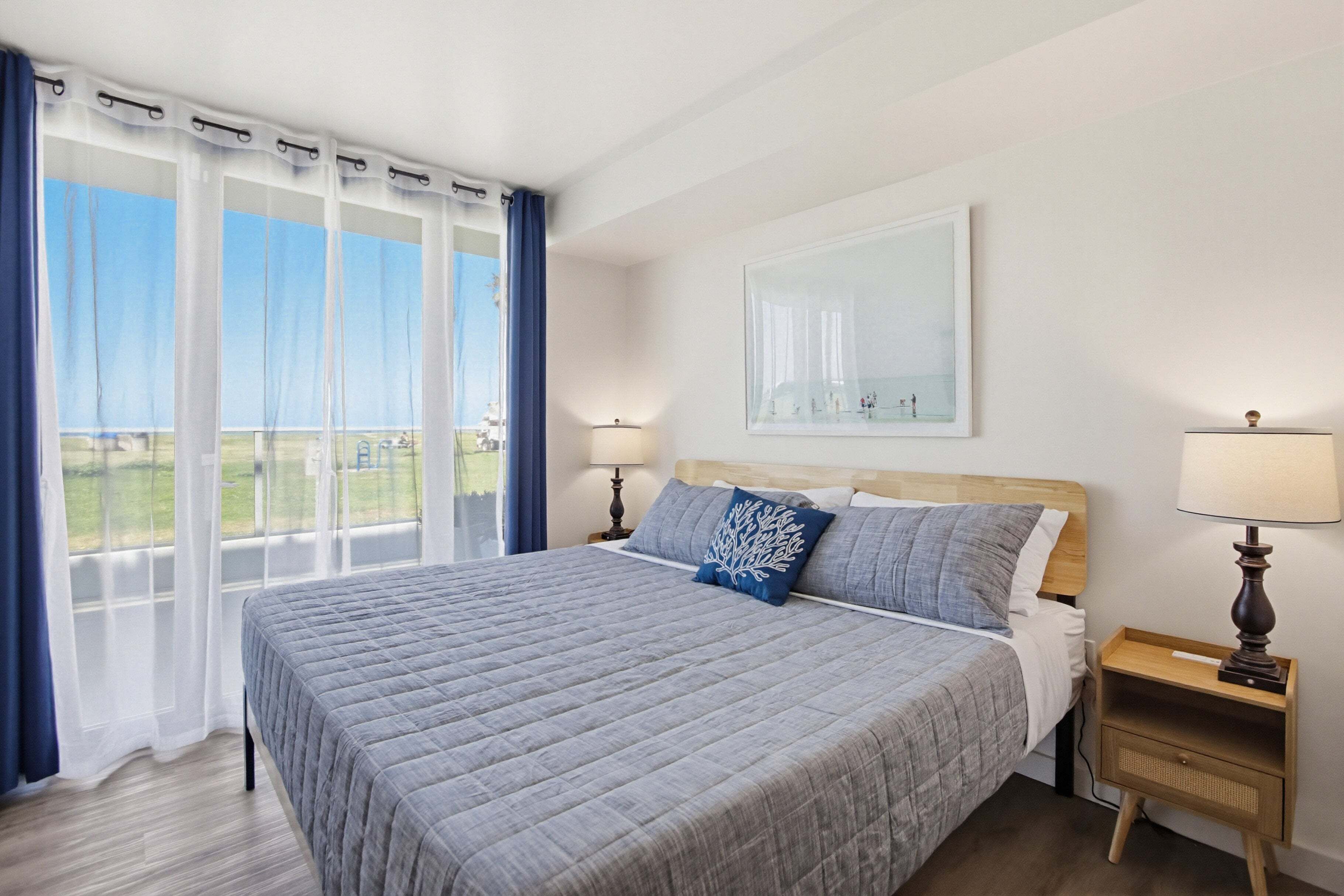 A bedroom with a large bed, two bedside tables, a window with curtains, and a painting on the wall.
