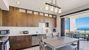 A modern kitchen with wooden cabinets, a dining area with a wooden table and chairs, and a view of the ocean. - Stylish Ocean Front Condo with Great Views (San Diego)