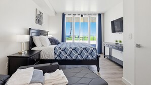 A modern bedroom with a bed, bedside table, TV, and a view of the outdoors.