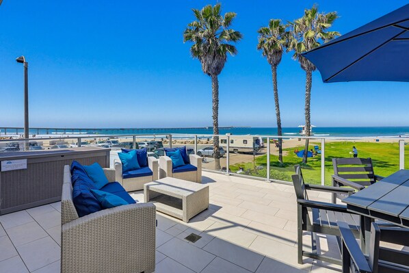 Una terraza en la azotea con mobiliario de mimbre, palmeras y vistas a la playa.