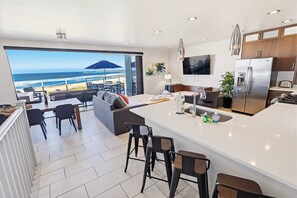 A modern hotel room with a large balcony, a kitchen with a refrigerator, and a dining area with a view of the beach.