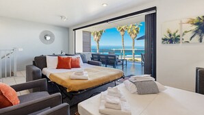Habitación de hotel con cama, escritorio, silla y balcón con vista al océano y palmeras.