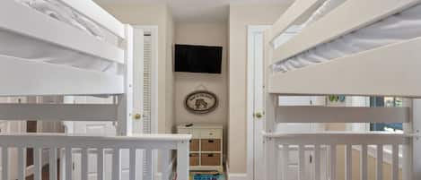 Een slaapkamer met stapelbedden, een televisie aan de muur en een kleine dressoir met lades.