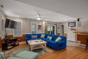A living room with a blue sectional sofa, a coffee table, a flat-screen TV mounted on the wall, and a sliding glass door leading to a patio.