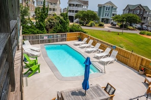 A rectangular swimming pool with a wooden deck, surrounded by lounge chairs and a blue umbrella. - Bella Vita: Pool, hot tub, volleyball/basketball, rec room, easy beach access! (Nags Head)