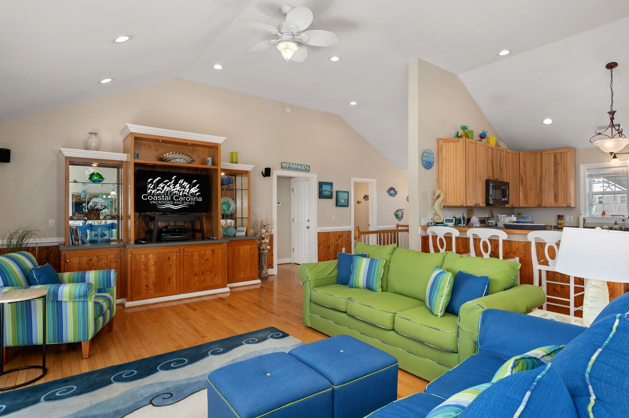 A spacious living room with a green sofa, blue armchairs, and a wooden entertainment center.