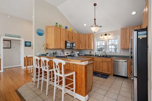 A kitchen with wooden cabinets, a central island with bar stools, a microwave, and a refrigerator.