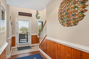 A hallway with a wooden floor, a blue rug, a staircase with white railings, and a wall decoration of fish. - Bella Vita: Pool, hot tub, volleyball/basketball, rec room, easy beach access! (Nags Head)