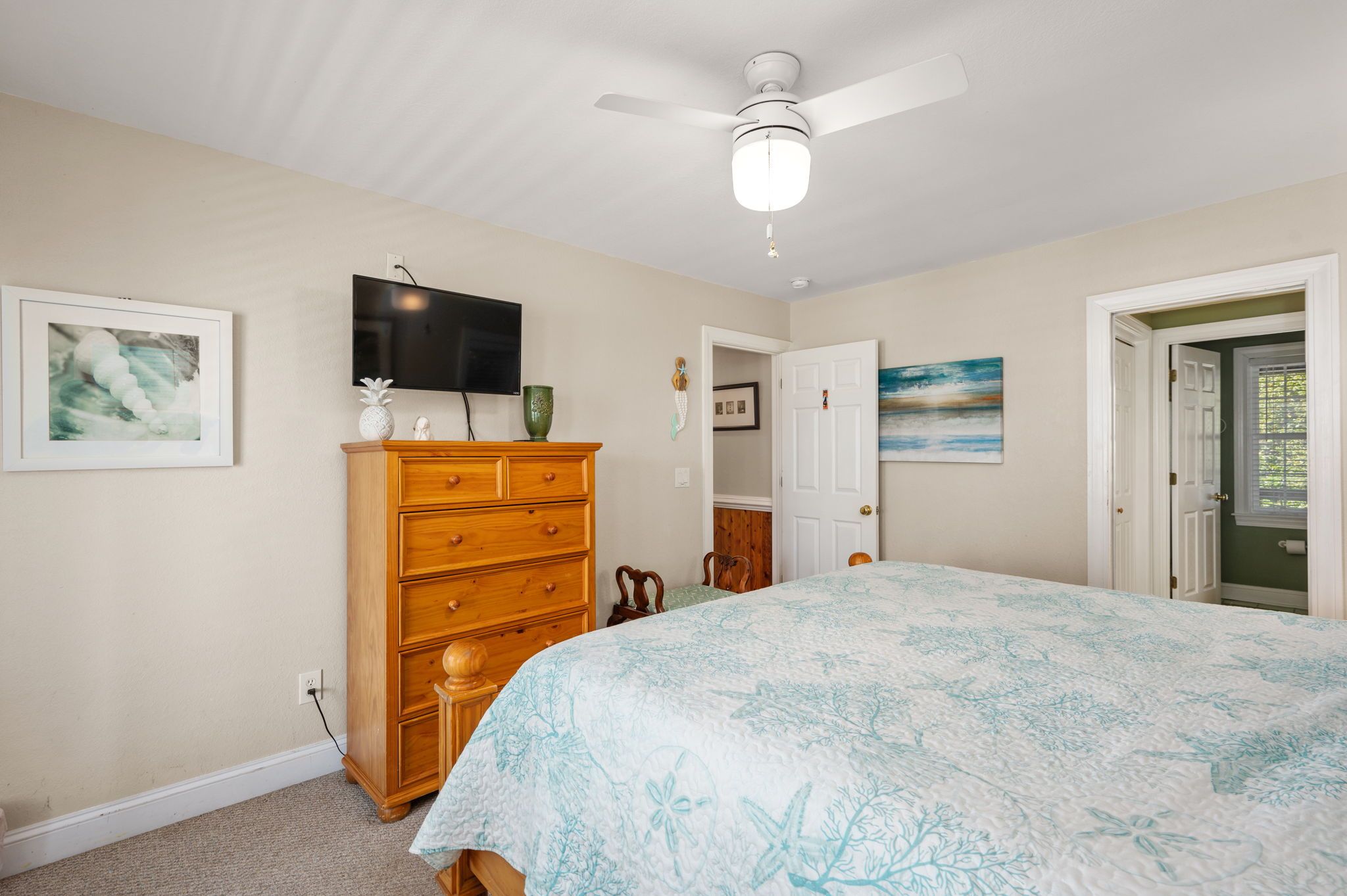 A bedroom with a bed, a dresser, a television, and a ceiling fan.