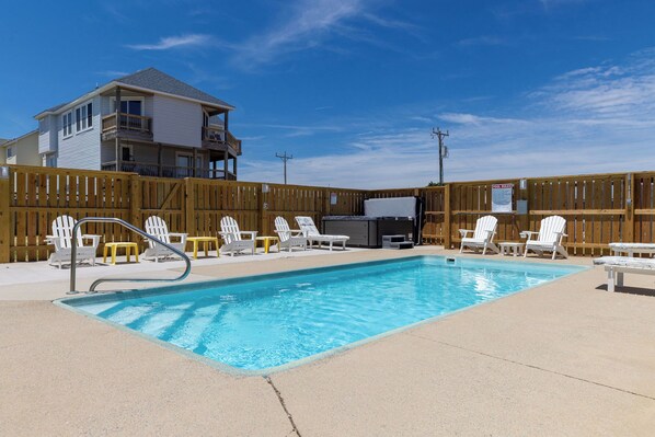 Une piscine dotée de chaises longues et d’un jacuzzi, le tout entouré d’une clôture en bois.
