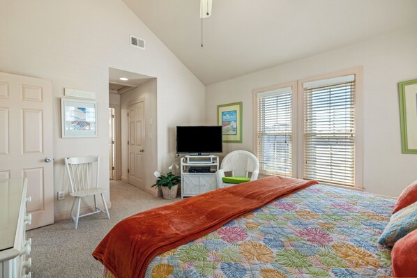 A bedroom with a bed, a television, a chair, and a window with blinds.