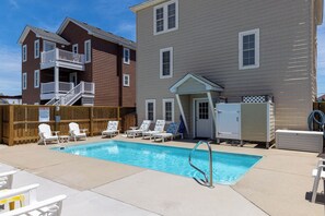 A swimming pool with lounge chairs and a covered area, surrounded by two-story buildings.