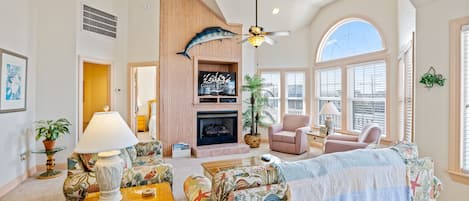 A spacious living room with a fireplace, a ceiling fan, and a large window.