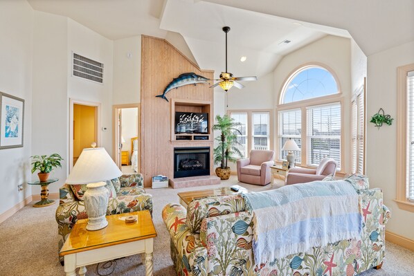 A spacious living room with a fireplace, a ceiling fan, and a large window.
