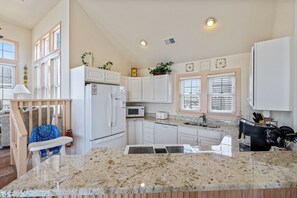 A modern kitchen with white cabinetry, a granite countertop, a built-in microwave, and a stainless steel sink. - Ocean Escape: Oceanside, pool, hot tub, pool table, easy beach access (Kill Devil Hills)