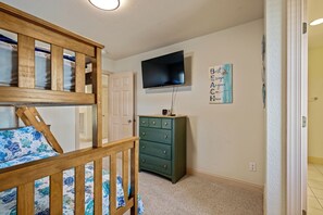 Une chambre avec un lit superposé, une commode, un téléviseur à écran plat et un élément décoratif mural.