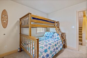 A bunk bed with a wooden ladder, a window with blinds, and a door leading to a staircase.