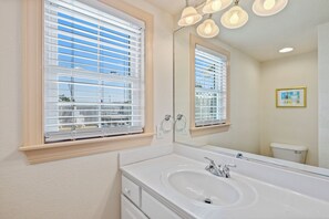 Une salle de bain avec un grand miroir, un lavabo blanc et une fenêtre avec des stores.