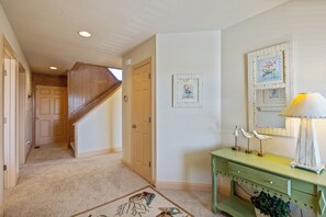 A hallway with a carpeted floor, a wooden staircase, and a green console table with a lamp.