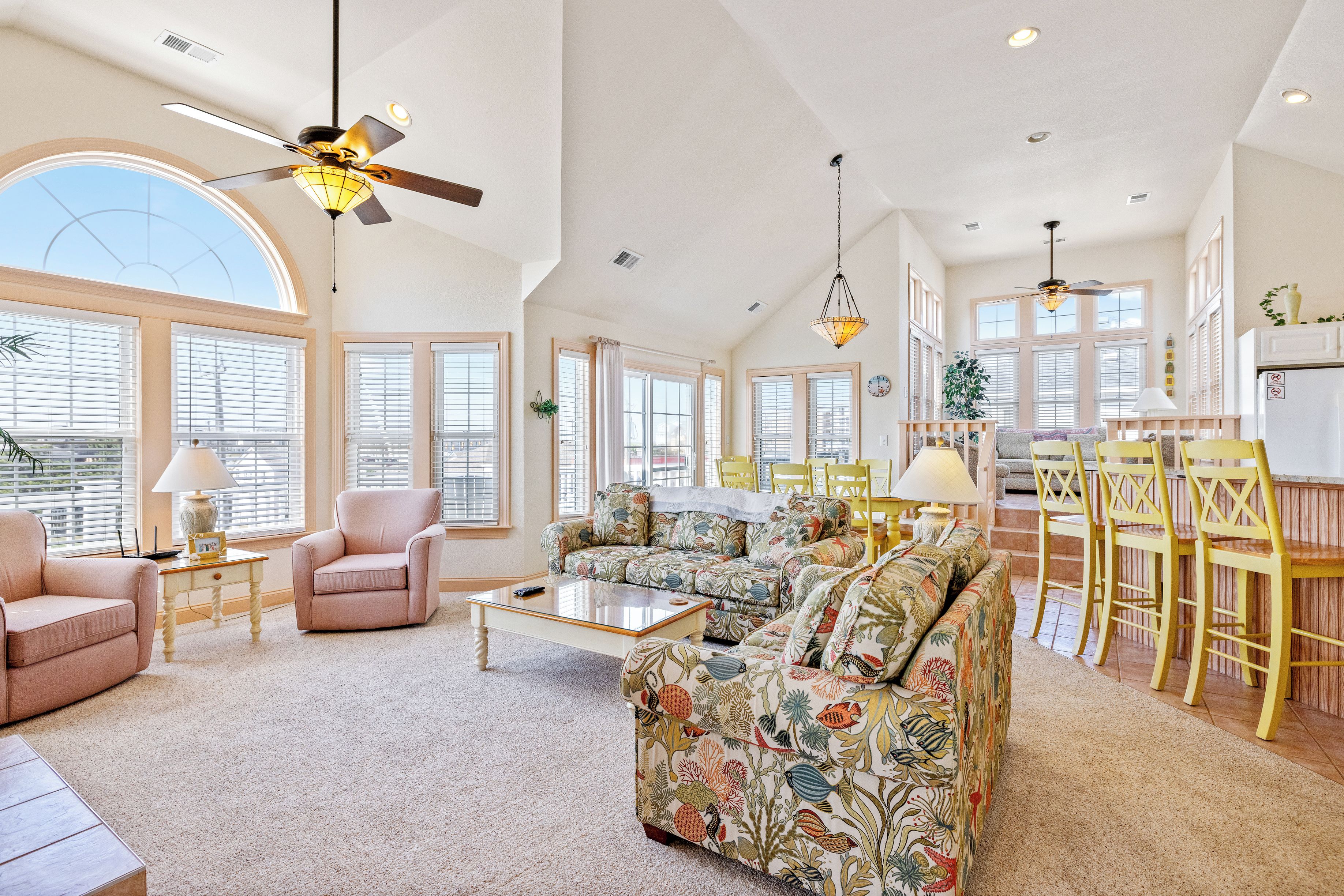 A spacious living room with a large sofa, a coffee table, and a dining area with yellow chairs.