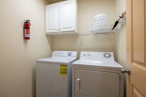 A laundry room with two washing machines, a fire extinguisher, and a shelf with a basket.