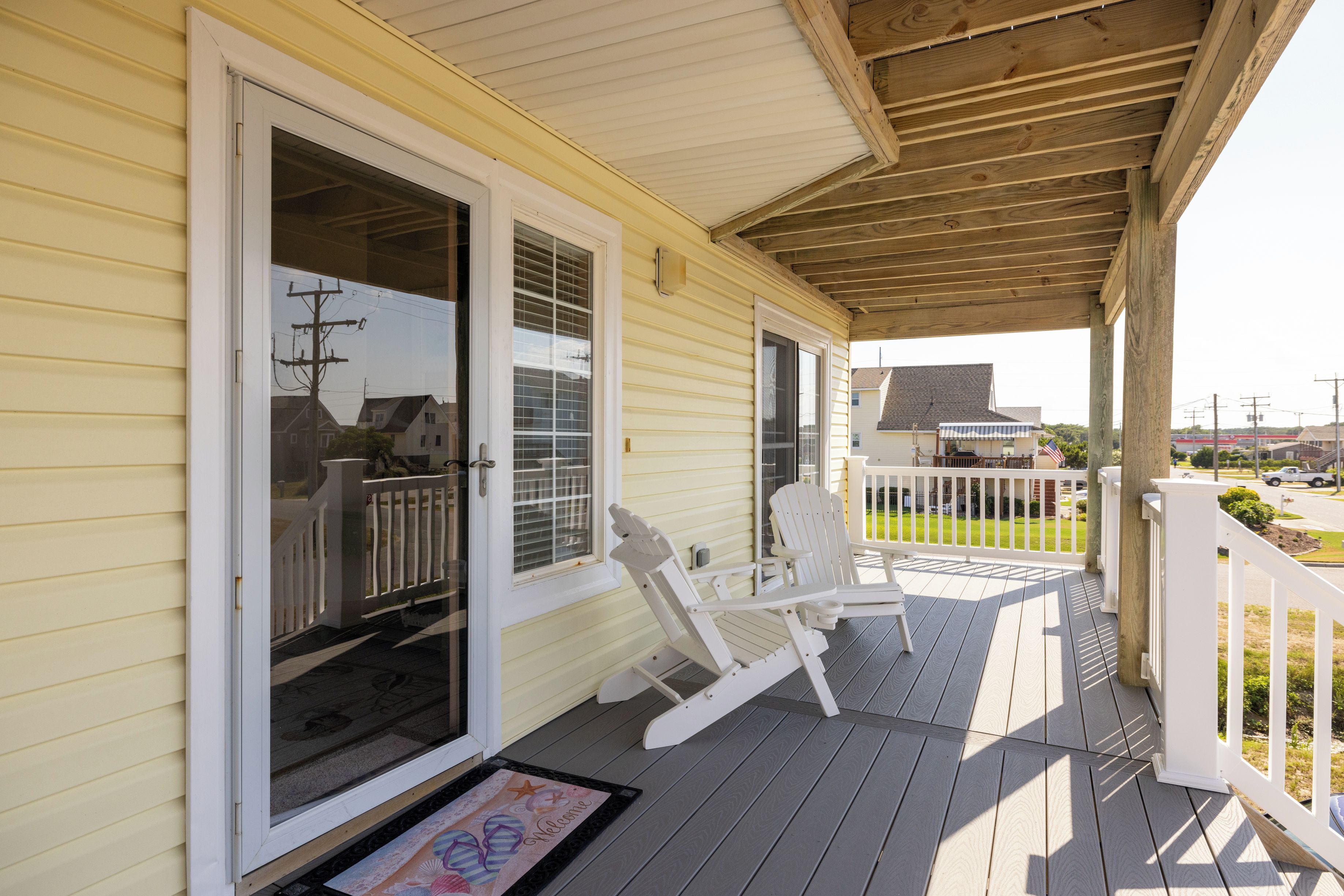 A covered porch with a wooden railing, a sliding glass door, and two Adirondack chairs.