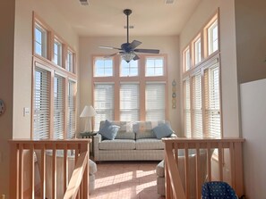 A sunlit room with a ceiling fan, a sofa with cushions, and a small table. - Ocean Escape: Oceanside, pool, hot tub, pool table, easy beach access (Kill Devil Hills)