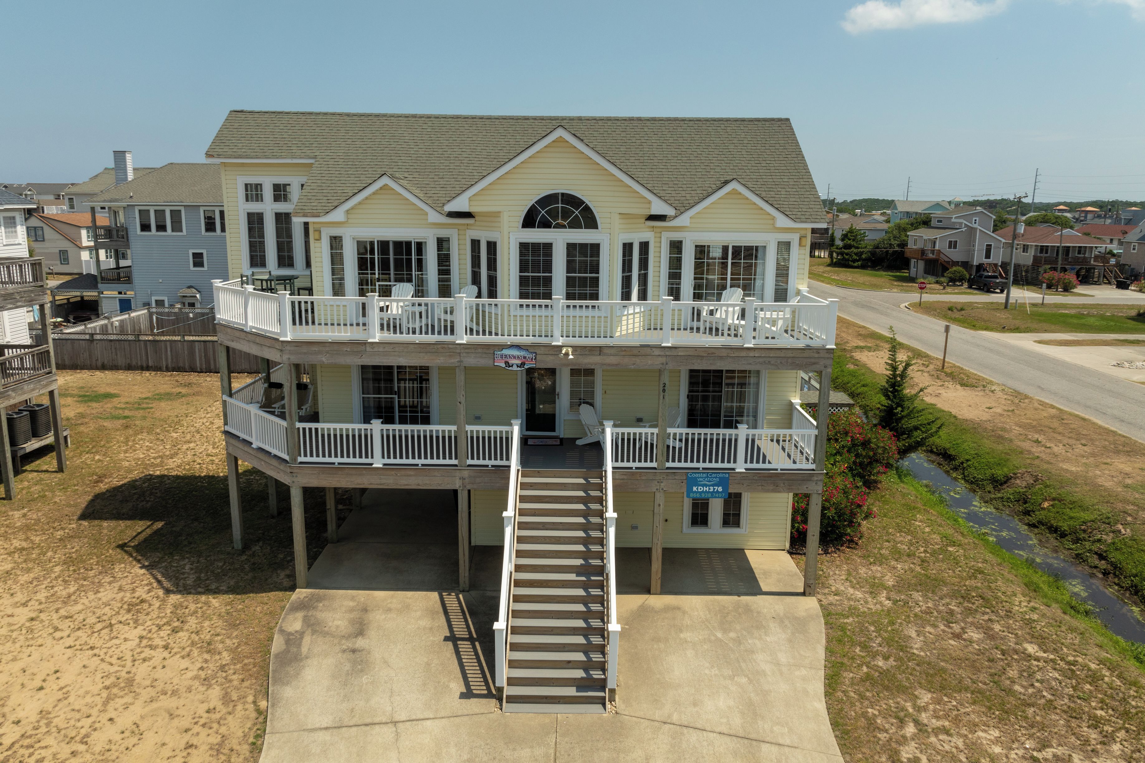 A two-story waterfront property with a balcony, a covered deck, and a staircase leading to the entrance.