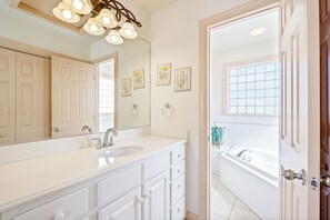 Une salle de bain avec un grand miroir, un meuble-lavabo blanc et une baignoire.