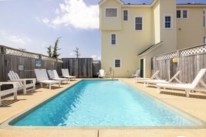 A rectangular swimming pool with a wooden deck and lounge chairs.