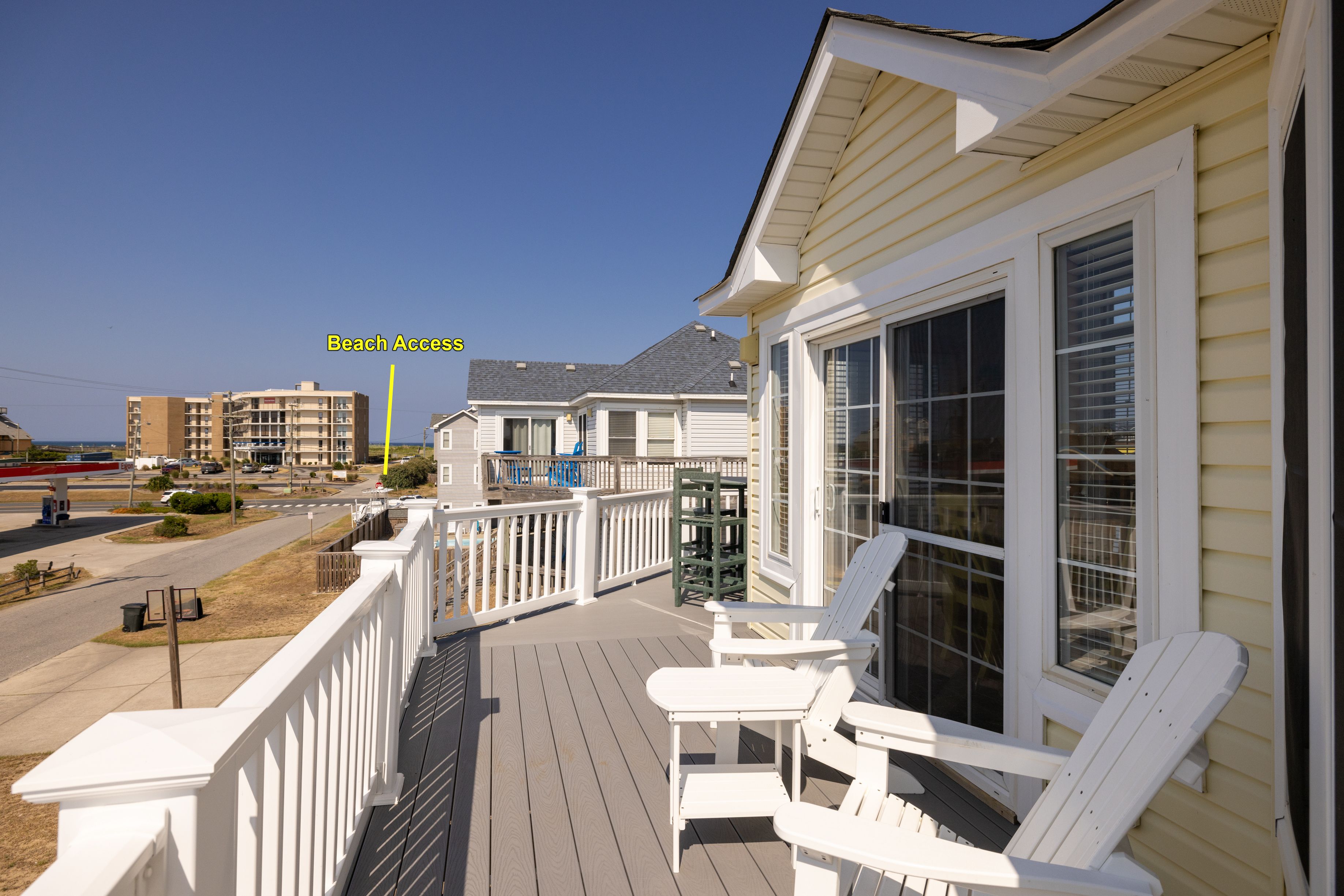 A beachfront property with a deck, white outdoor furniture, and a view of the beach.
